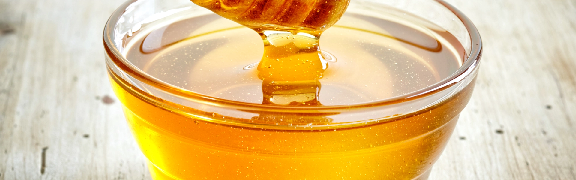 organic thick honey dripping from the honey dipper in a glass bowl